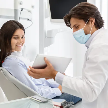 a woman sitting in a dentist chair with a doctor holding a tablet